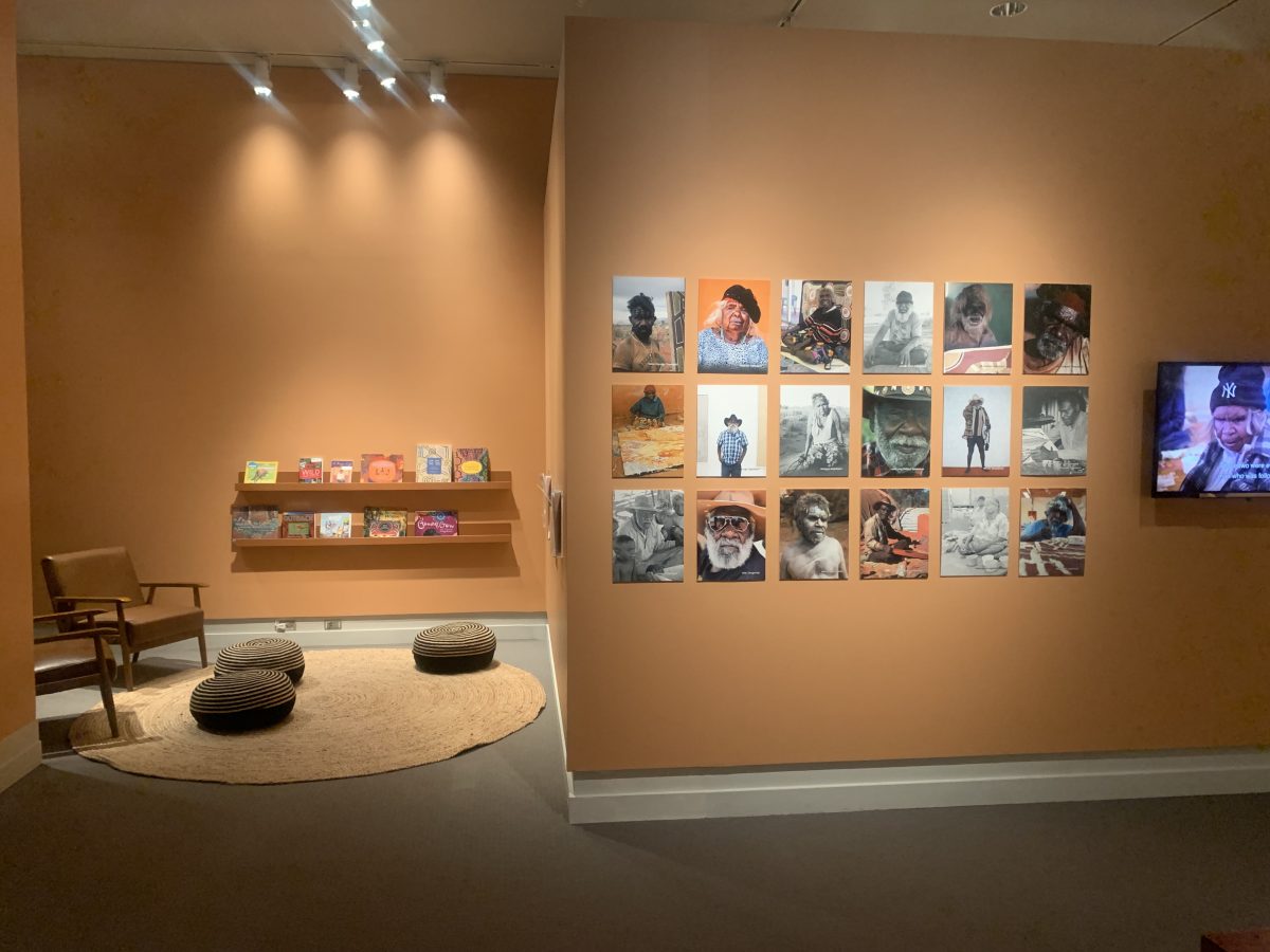 Interactive gallery space with a reading area, children’s books on display, and a photo grid of Aboriginal artists on the wall.