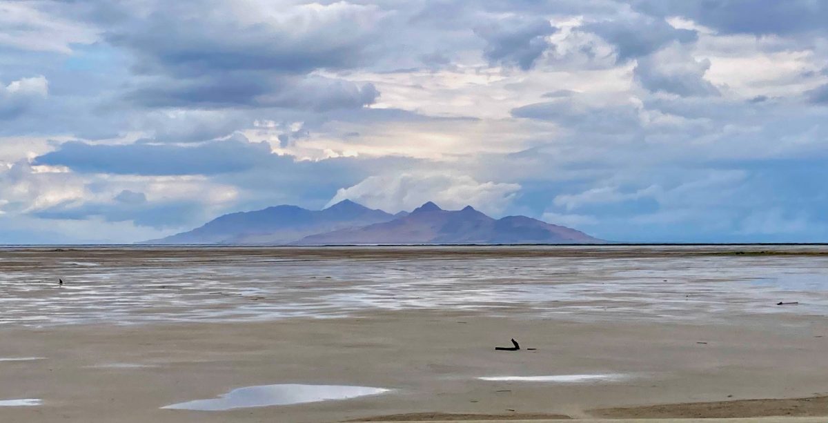 Great Salt Lake under stormy skies with Antelope Island in the distance, showing receding water and exposed lakebed.