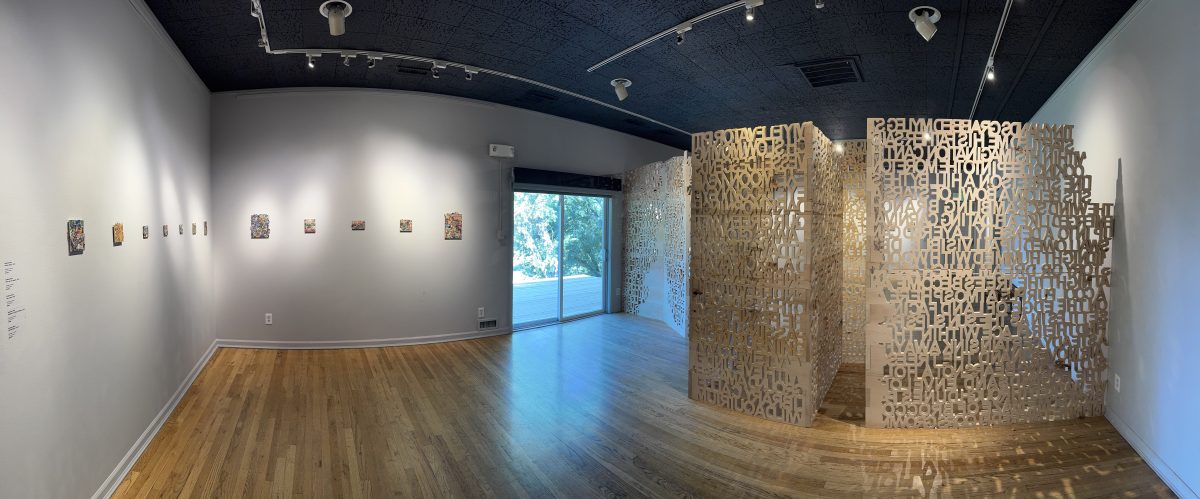 Gallery interior featuring a row of small collage artworks on a white wall opposite large wooden text panels forming a partition.