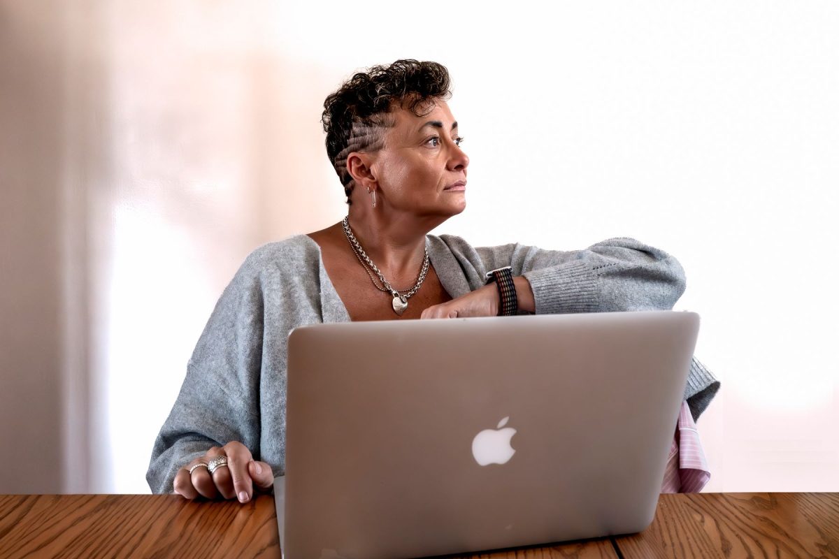 Actor Tamara Howell sitting at a table with an open laptop, looking thoughtfully out of frame.