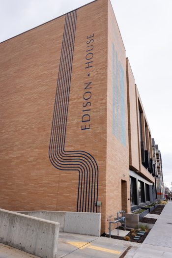 Exterior view of Edison House, a modern brick building with vertical blue linework and the club’s name displayed on the side.