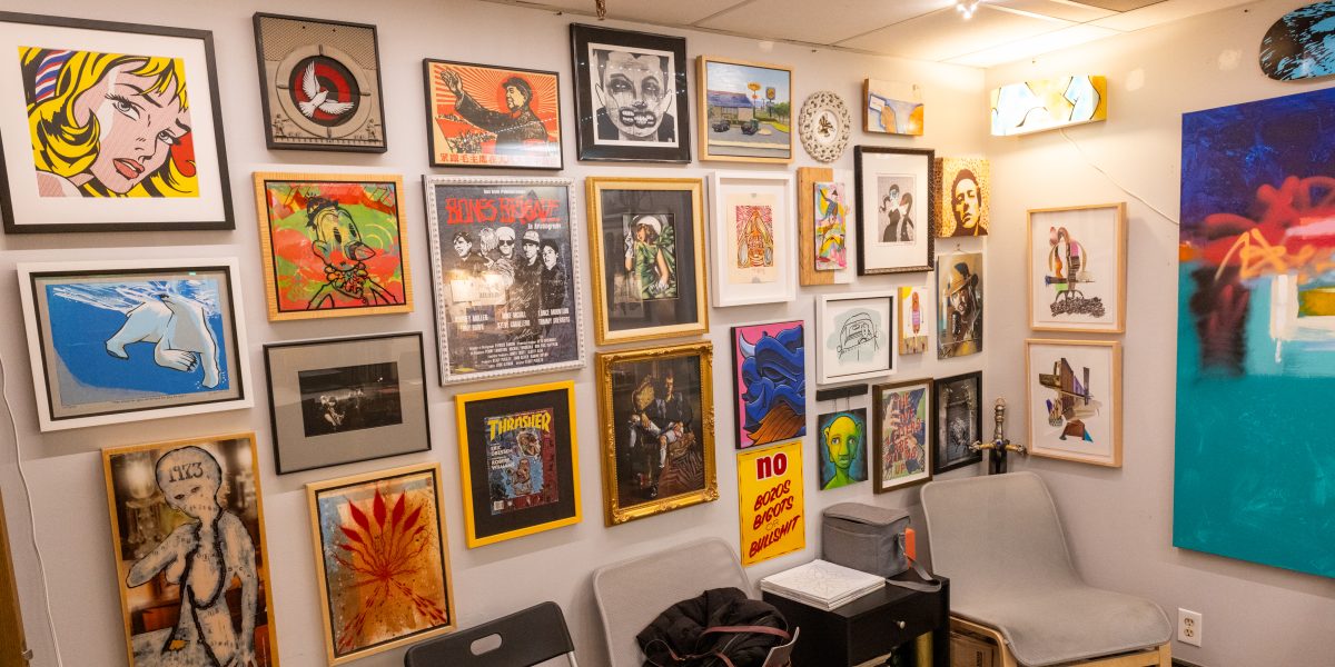 A gallery-style wall inside Harrington Art Studio filled with an eclectic mix of framed artworks, including pop art, illustration, photography, posters, and mixed-media pieces.