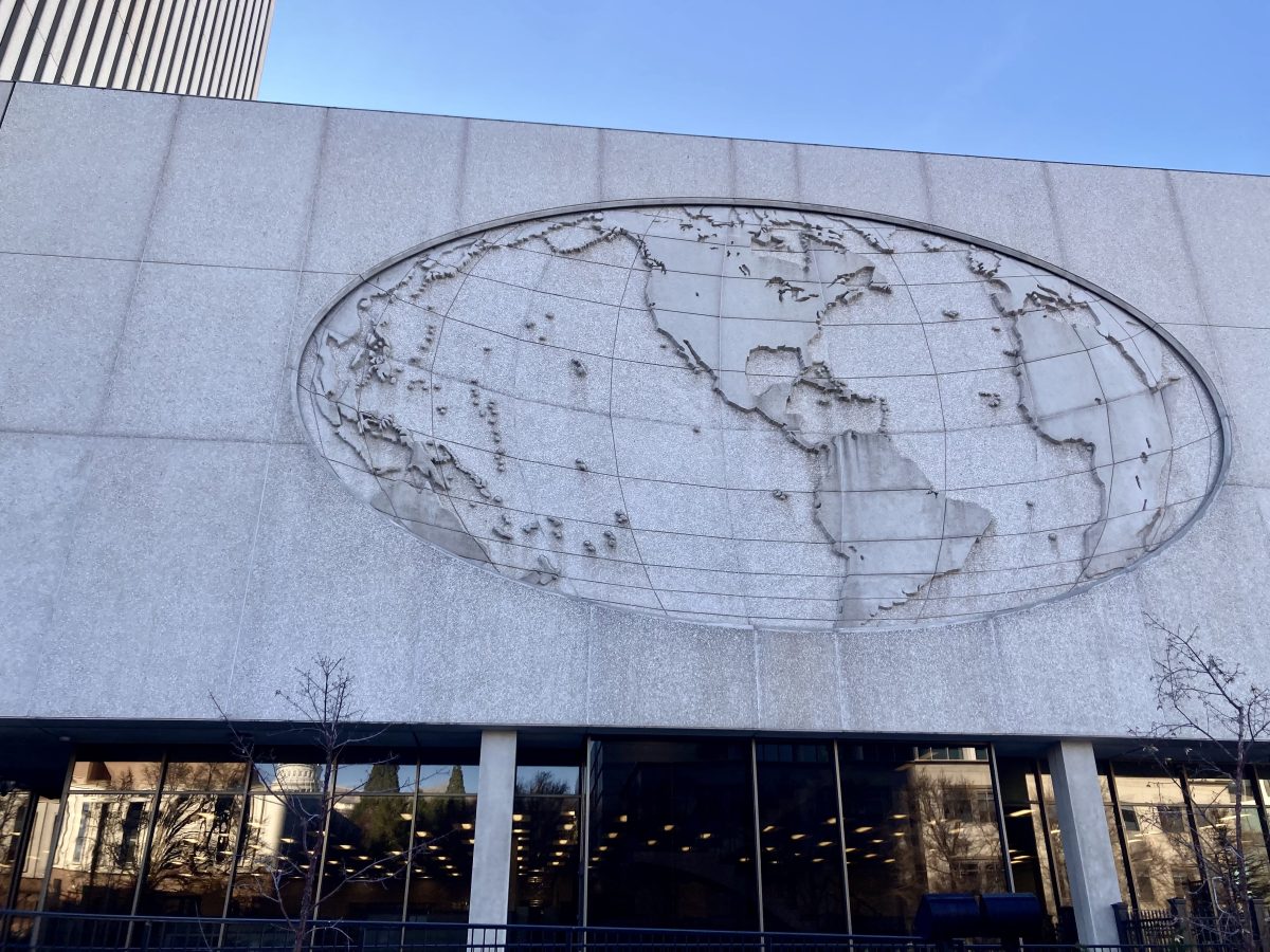 Shaded concrete oval world map relief on the north side of the LDS Church Office Building, showing the Americas and grid lines above a row of dark windows.