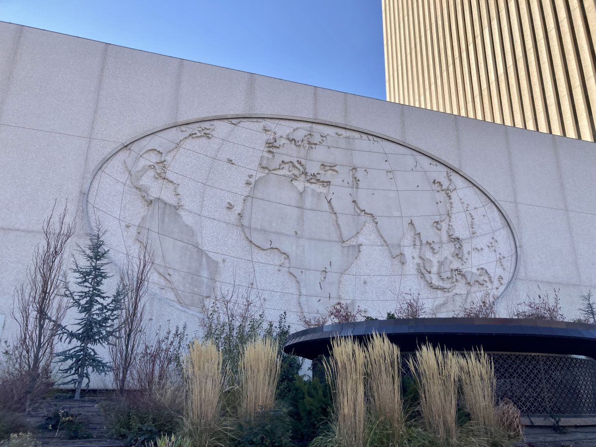 Angled view of the north-side concrete world map relief on the LDS Church Office Building, with the tall tower rising behind it and landscaping in the foreground.