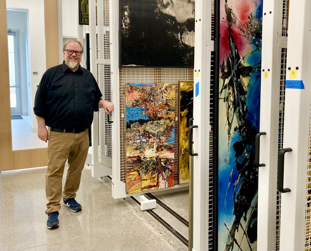 Man standing beside sliding art storage racks filled with paintings in a museum collection area.