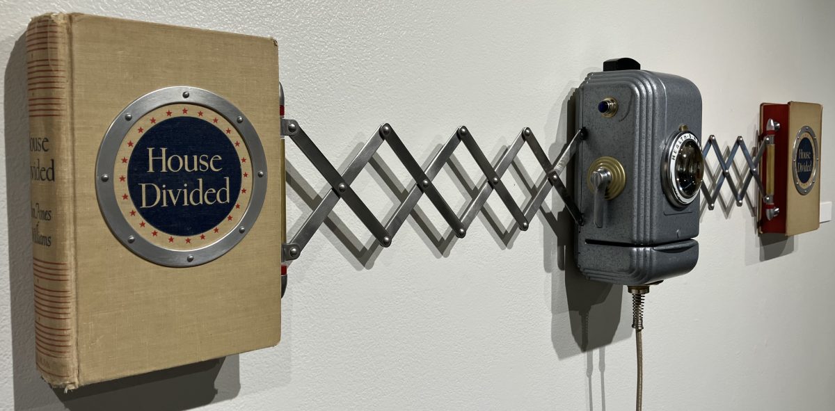 Close-up of a book titled “House Divided” attached to a metal accordion arm leading to a small mechanical viewing device mounted on a wall.