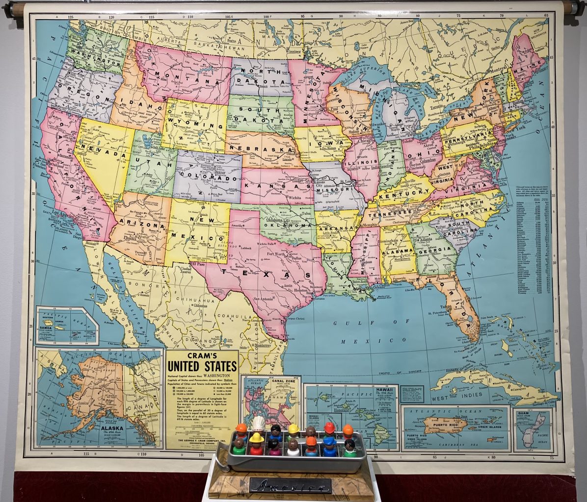 Large vintage map of the United States mounted on a wall, with a row of small colorful figurines displayed on a ledge in front.
