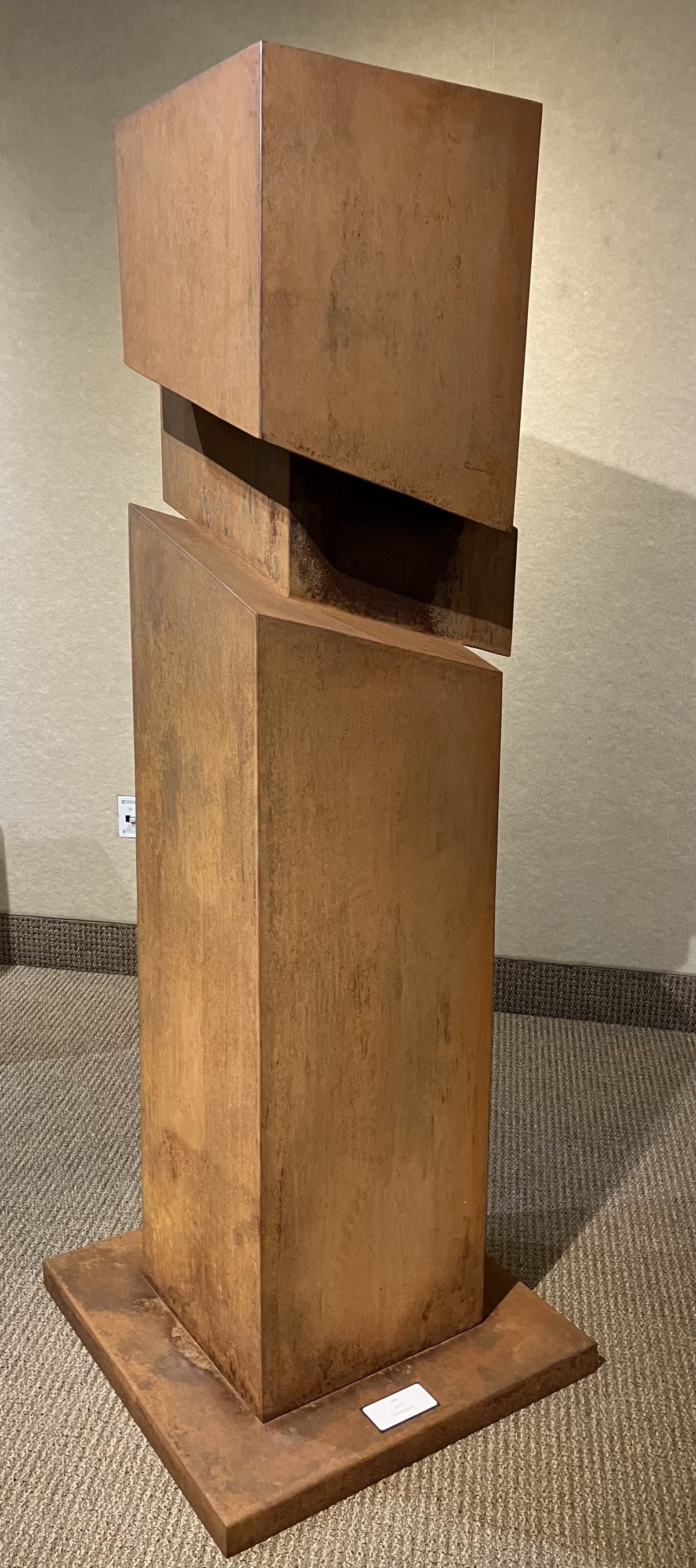 Abstract metal sculpture titled 'Shift' consisting of rust-colored geometric blocks stacked and slightly misaligned, creating a sense of dynamic movement.