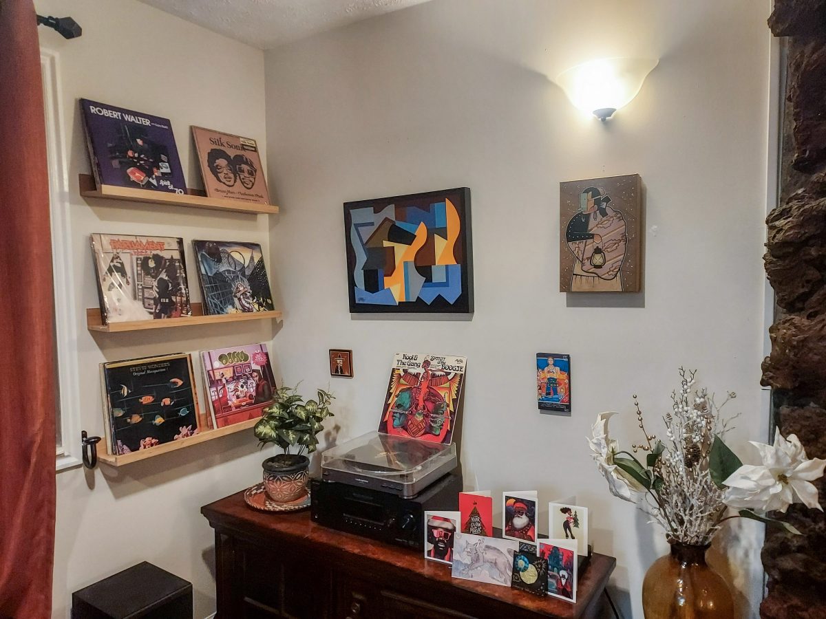 A room with a record player, vinyl albums displayed on shelves, framed abstract art, and decorative elements like plants and small figurines.