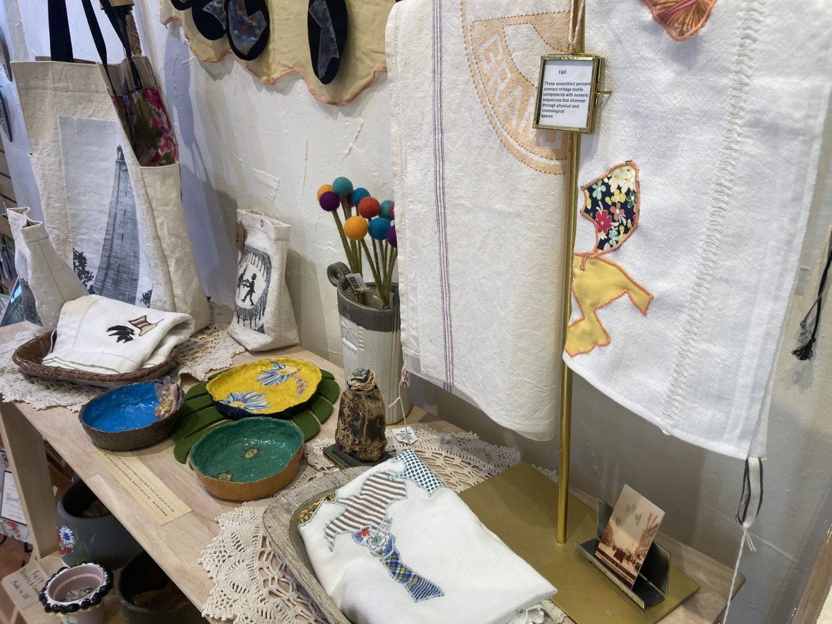Tabletop display featuring Fern & Reed’s printed totes, appliquéd textiles, and colorful ceramic bowls arranged on lace runners.