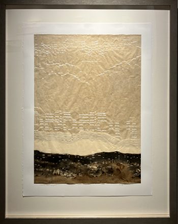 A vertical artwork composed of pale brown paper punched with musical notations above a desert floor rendered in ink and pigment, mounted within a large white mat.