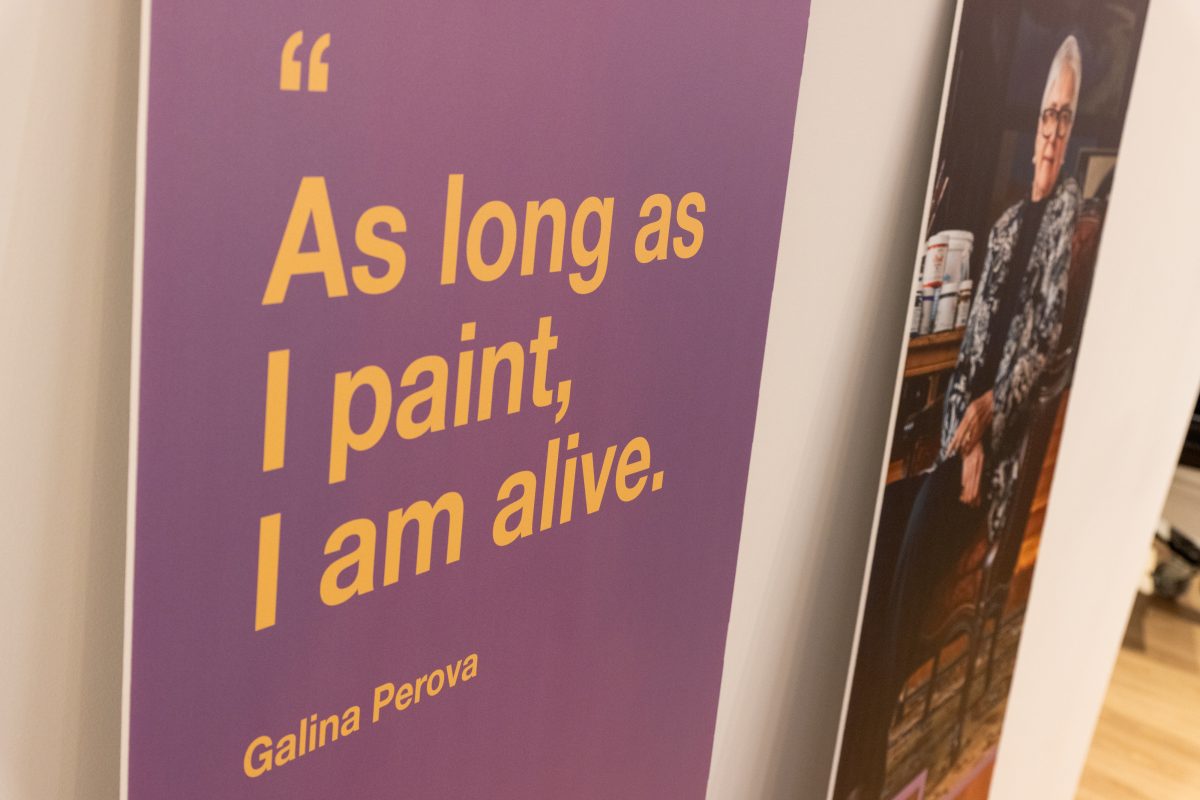 Exhibition wall with a purple panel displaying the quote “As long as I paint, I am alive.” by artist Galina Perova.