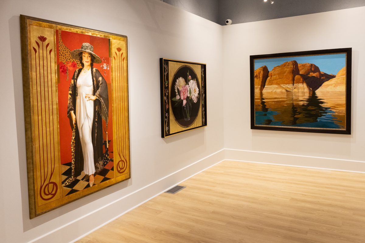 Corner view of three paintings in a gallery: a portrait of a woman in a white gown, a floral still life, and a desert landscape.