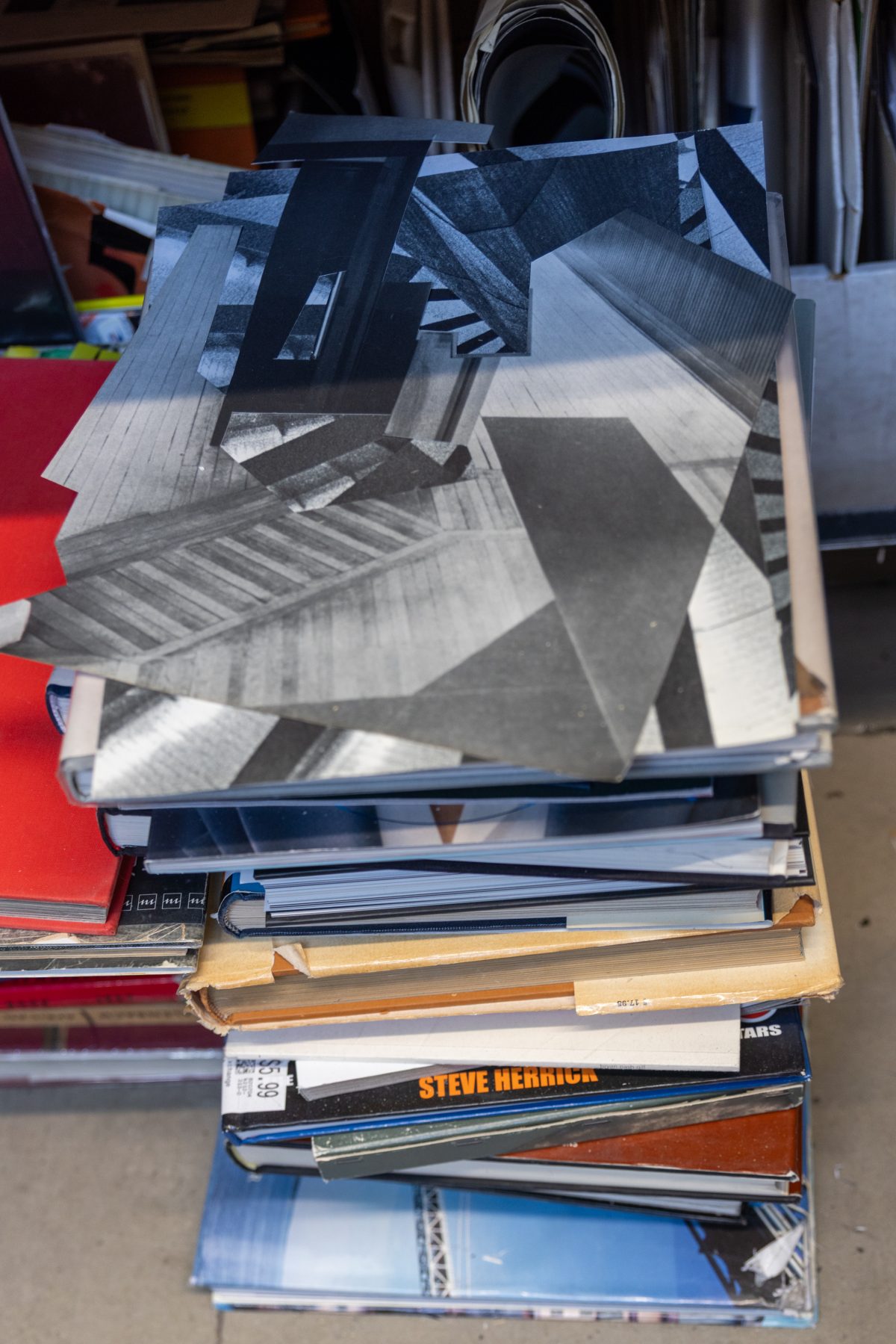 Stack of art books topped with a partially assembled black-and-white collage composed of architectural and geometric shapes.