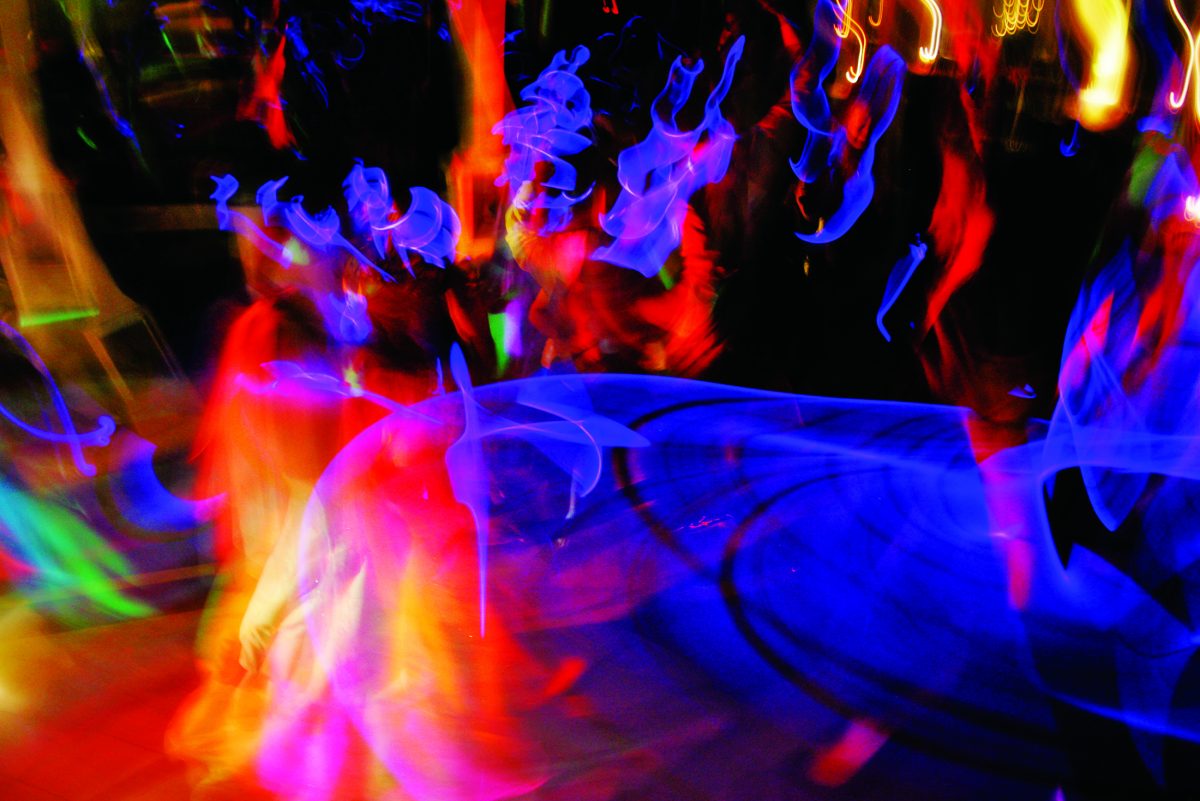 Abstract long-exposure photograph with swirling streaks of red, blue, and yellow light and blurred figures, creating a sense of movement and energy.