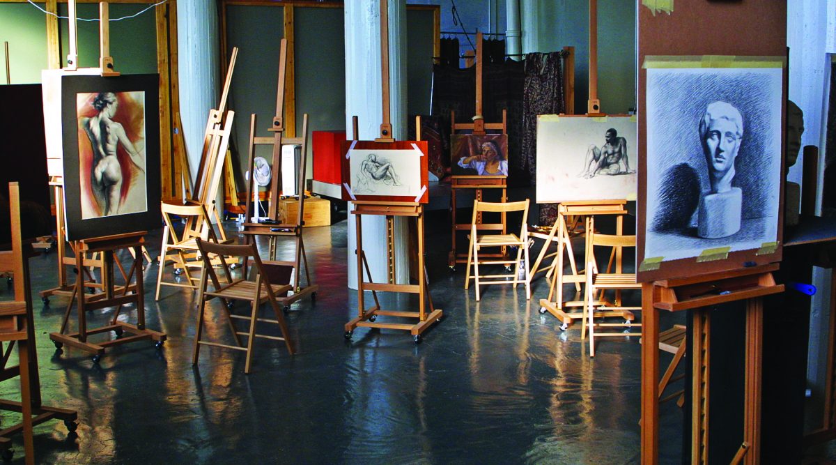 Art studio interior with multiple wooden easels holding figure drawings and paintings, with chairs arranged around them on a polished floor.