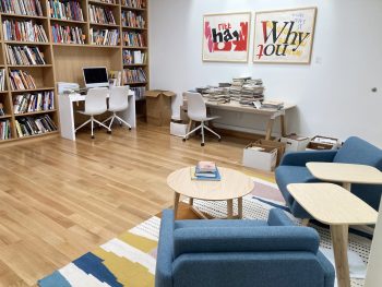 Library area with bookshelves, desks, chairs, and stacks of books in a museum research space.